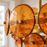 Close-up of the Velari Disc Orange Glass Chandelier showing textured amber glass discs, dark glass edges and gold-toned center fittings.