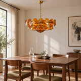 Velari Disc Orange Glass Chandelier with amber glass discs and gold hardware above a walnut dining table in a sunlit room.